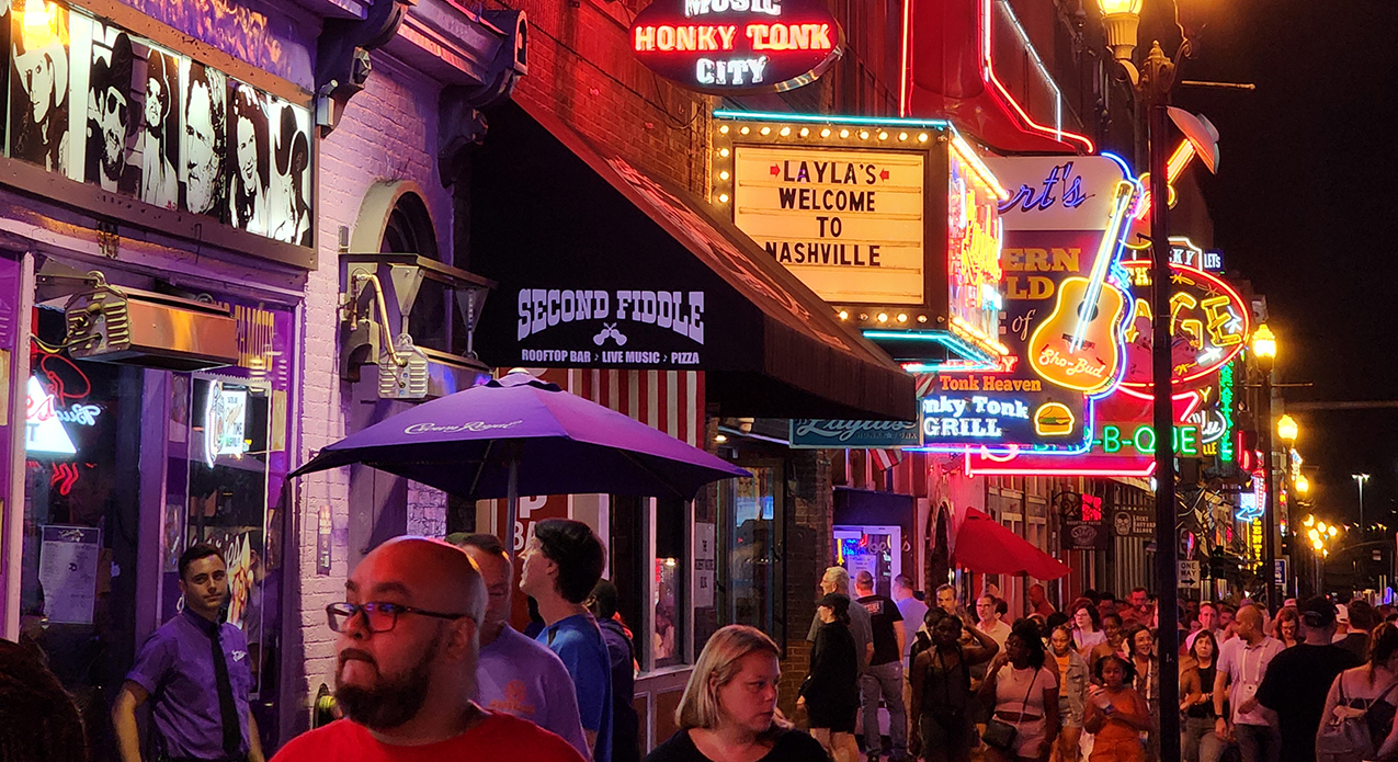 Lower Broadway at golden hour with neon signs and crowds