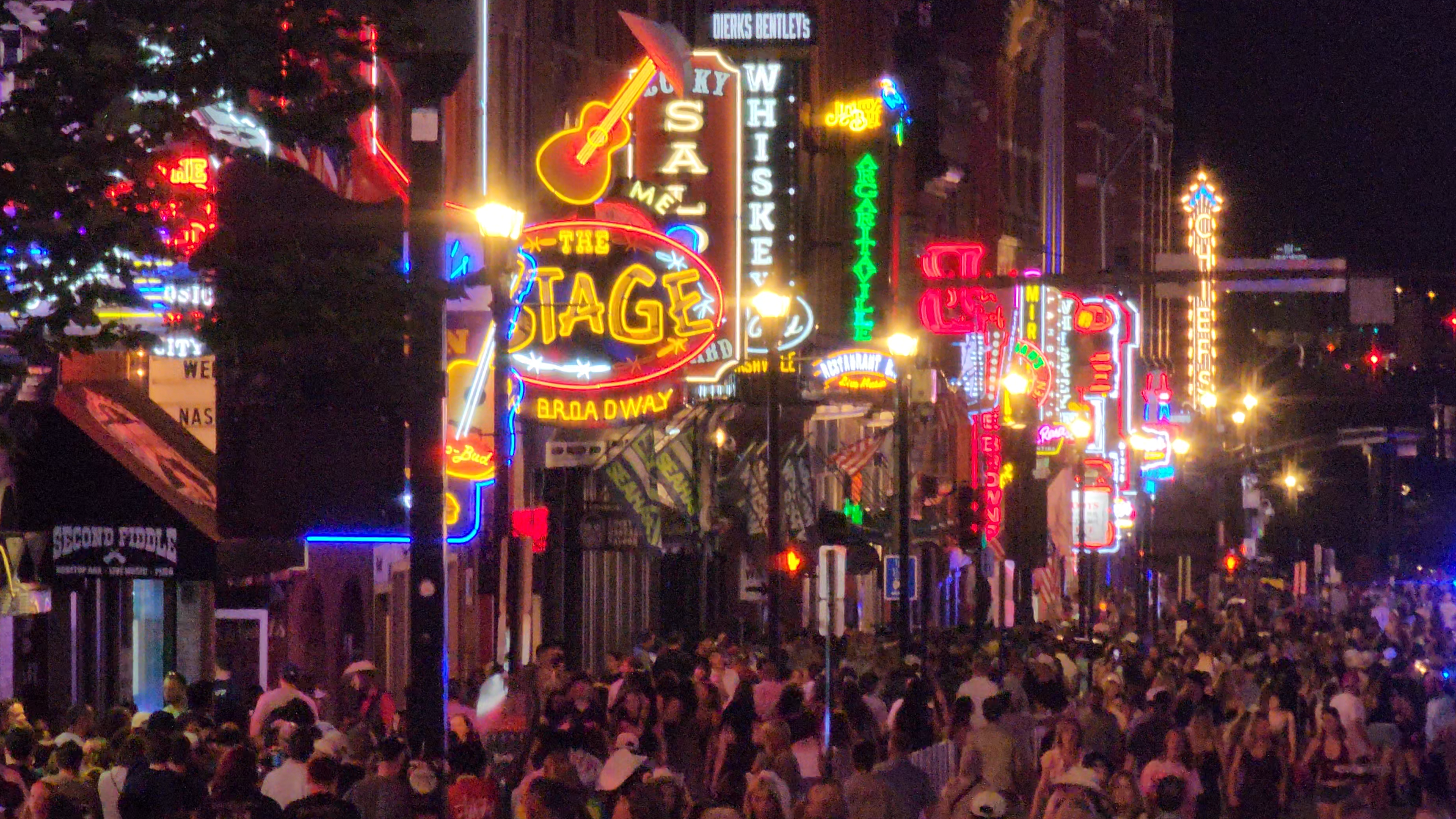 A dense late-night crowd beneath the neon honky-tonk signs on Lower Broadway.