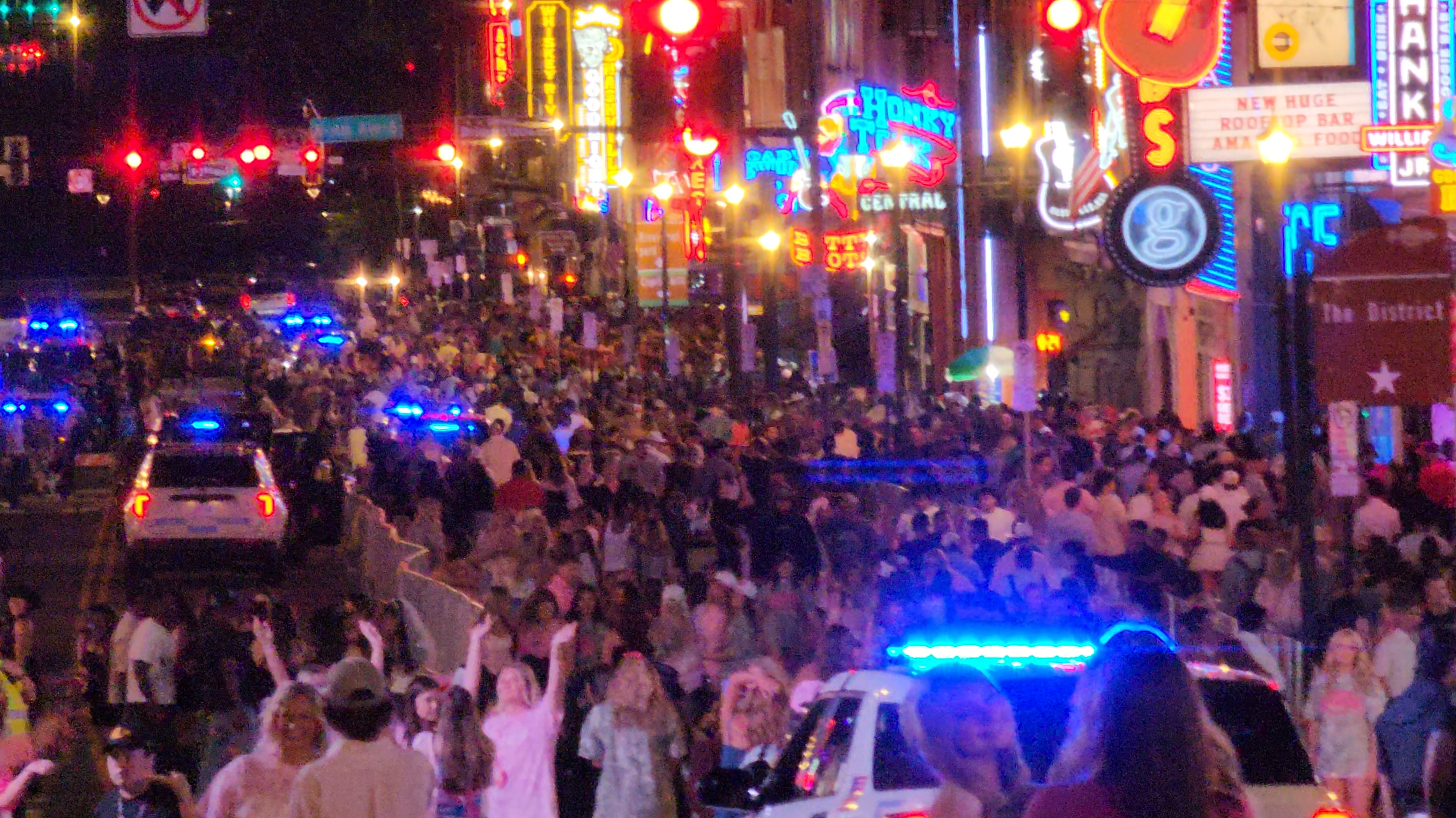 A very large nighttime crowd filling Lower Broadway as police vehicles move through the district.
