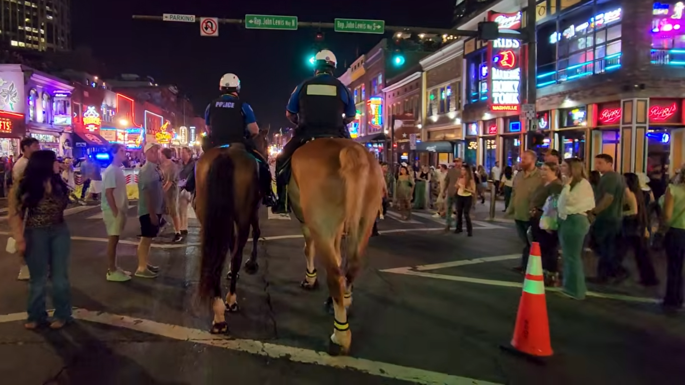 Two mounted police officers moving through a busy Lower Broadway intersection at night.