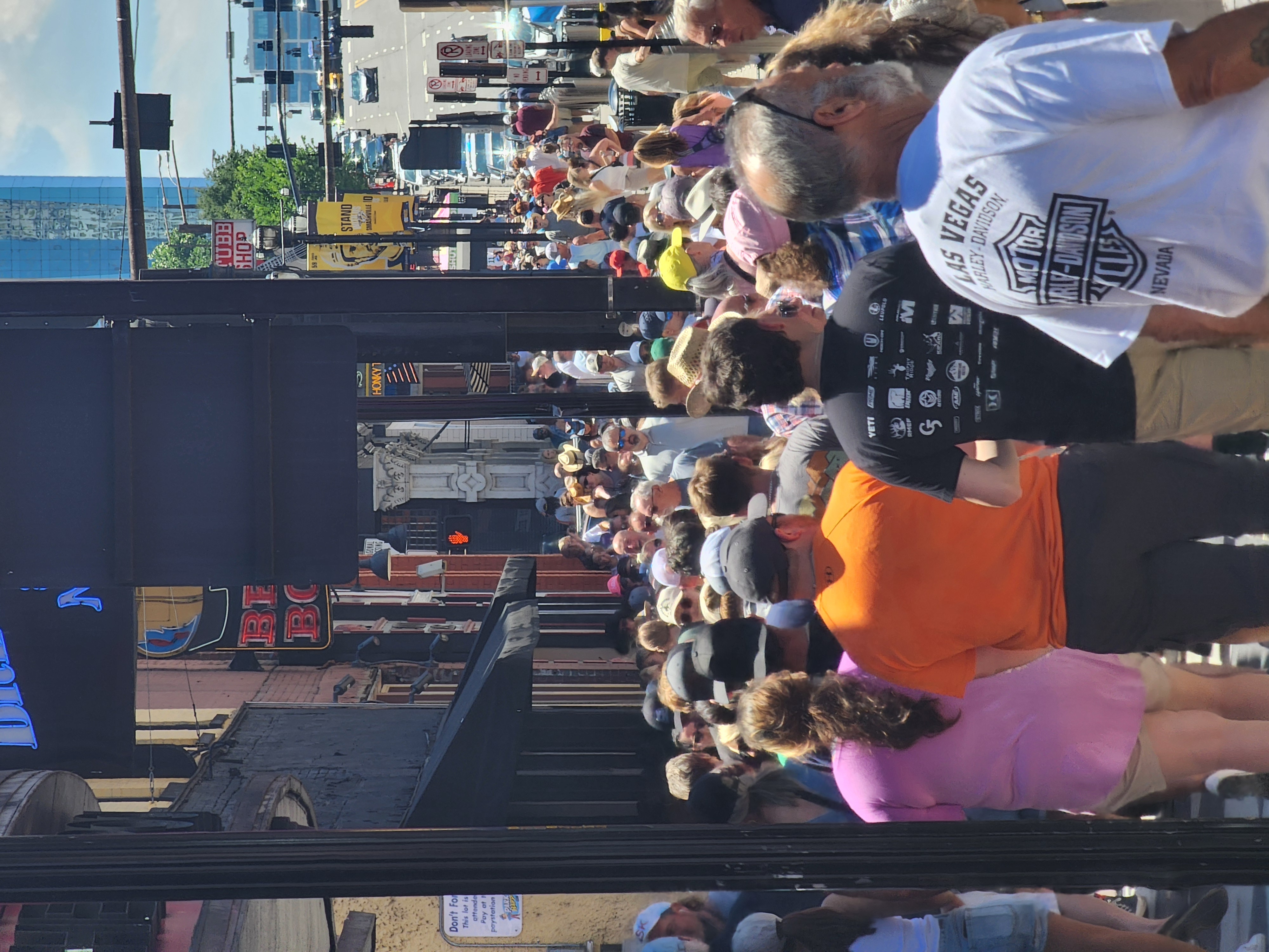 A dense daytime crowd walks along the sidewalk beneath Lower Broadway bar signs.