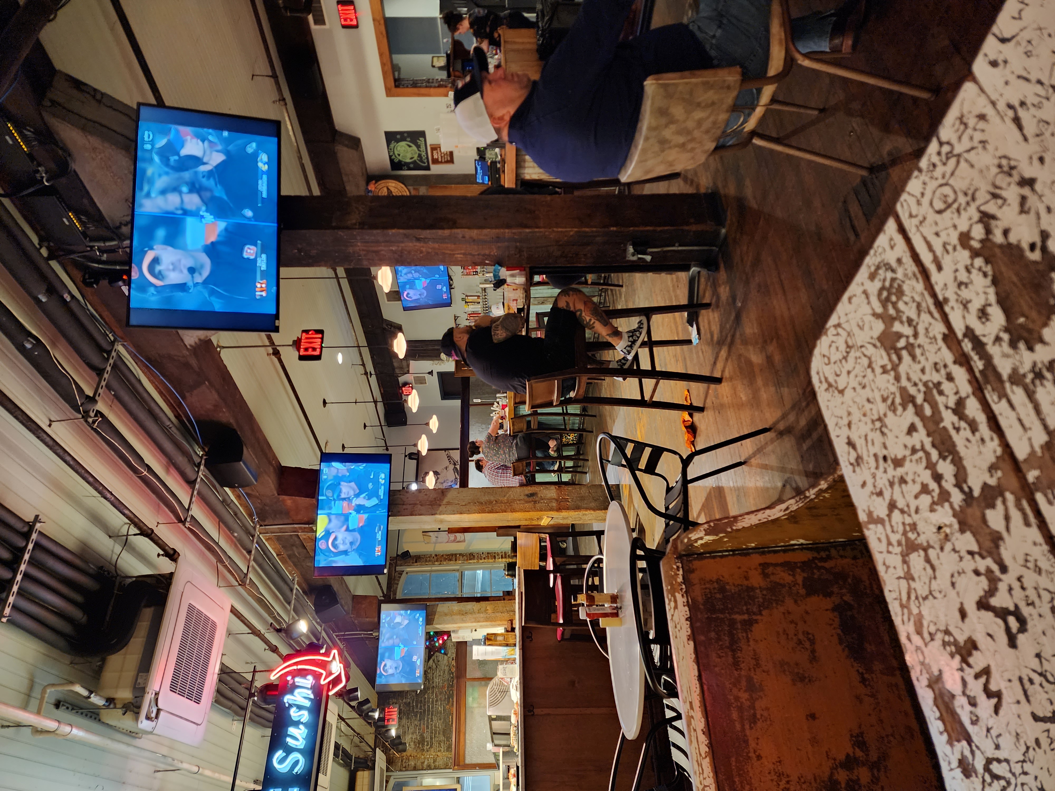 Several televisions show a football broadcast above tables and bar seating in a downtown bar.