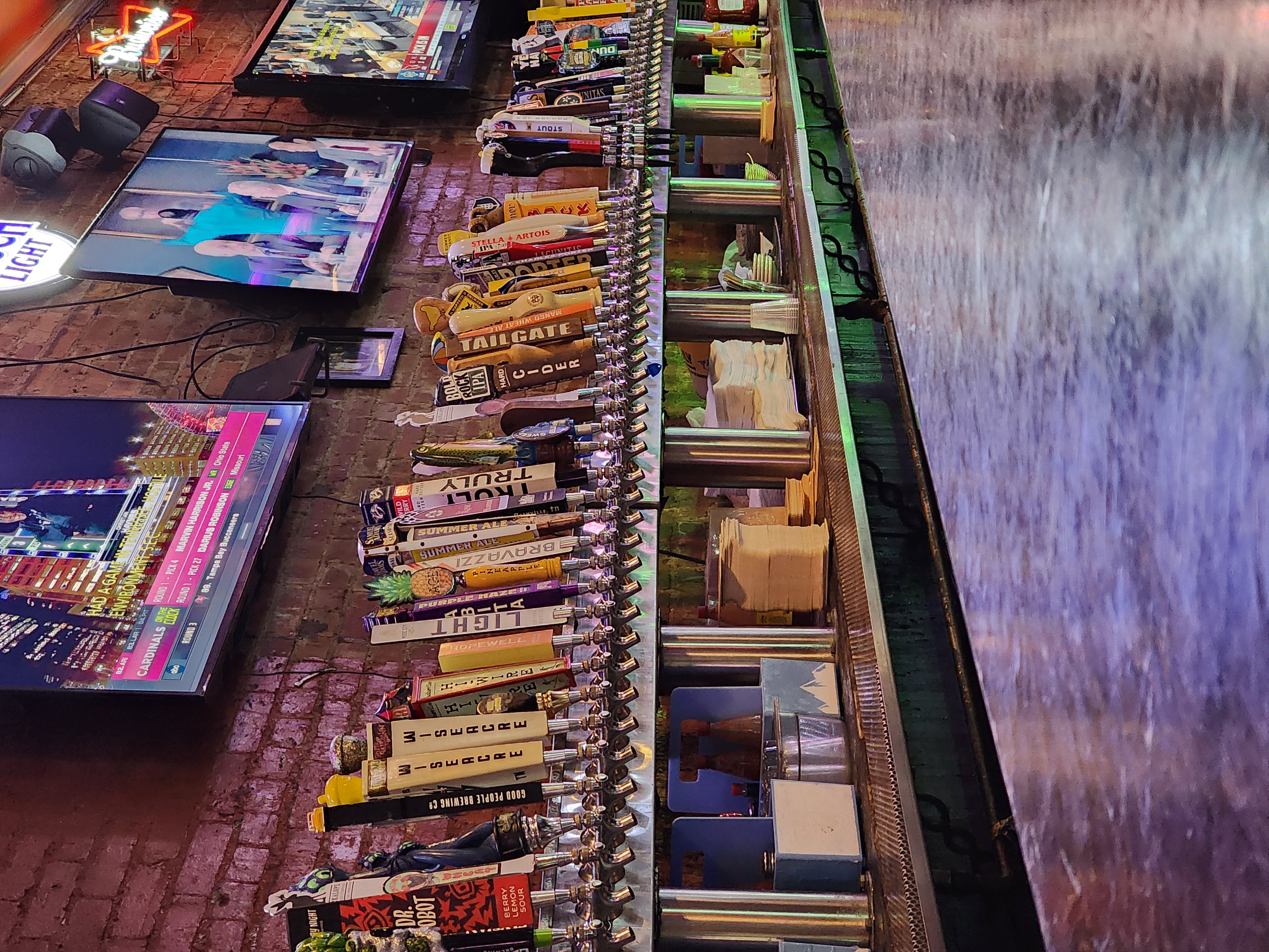 Televisions showing different programs hang above a long row of beer taps.