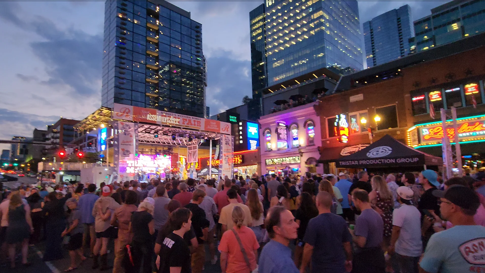 A crowd gathering on Lower Broadway as daylight fades and the neon begins to take over.