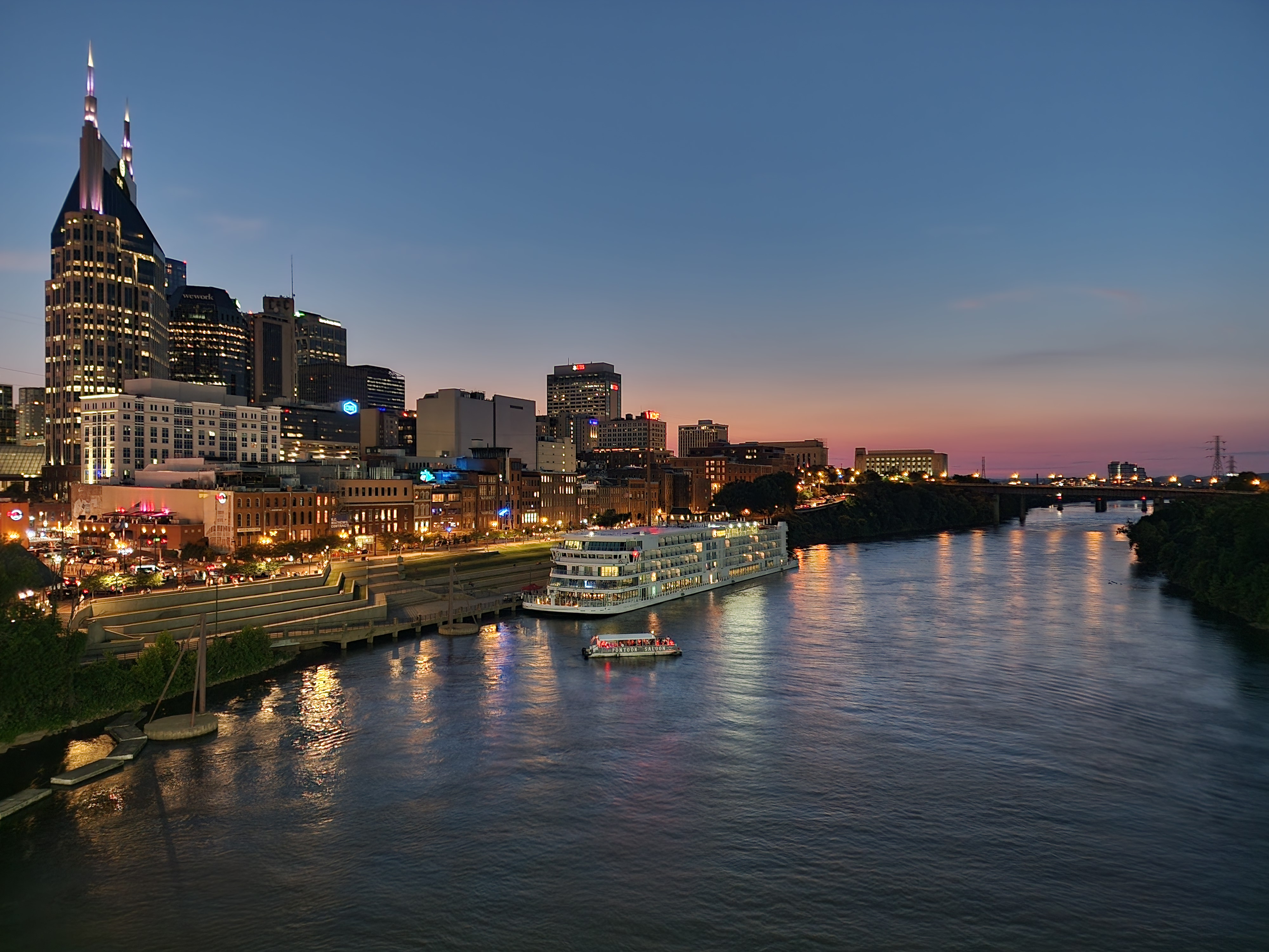The Nashville skyline and Riverfront Park beside the Cumberland River at dusk.