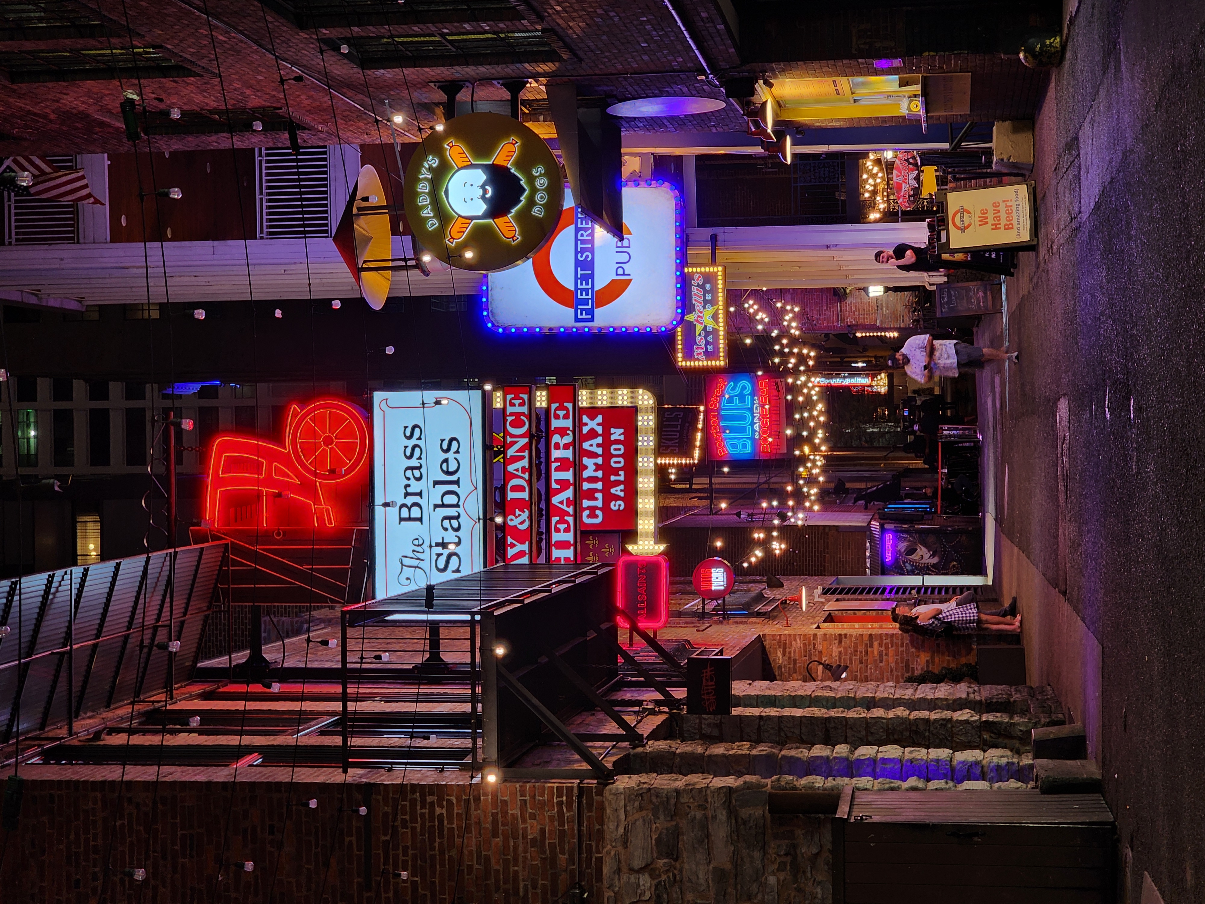 Neon signs and strings of lights illuminate the brick walls of Printer's Alley at night.