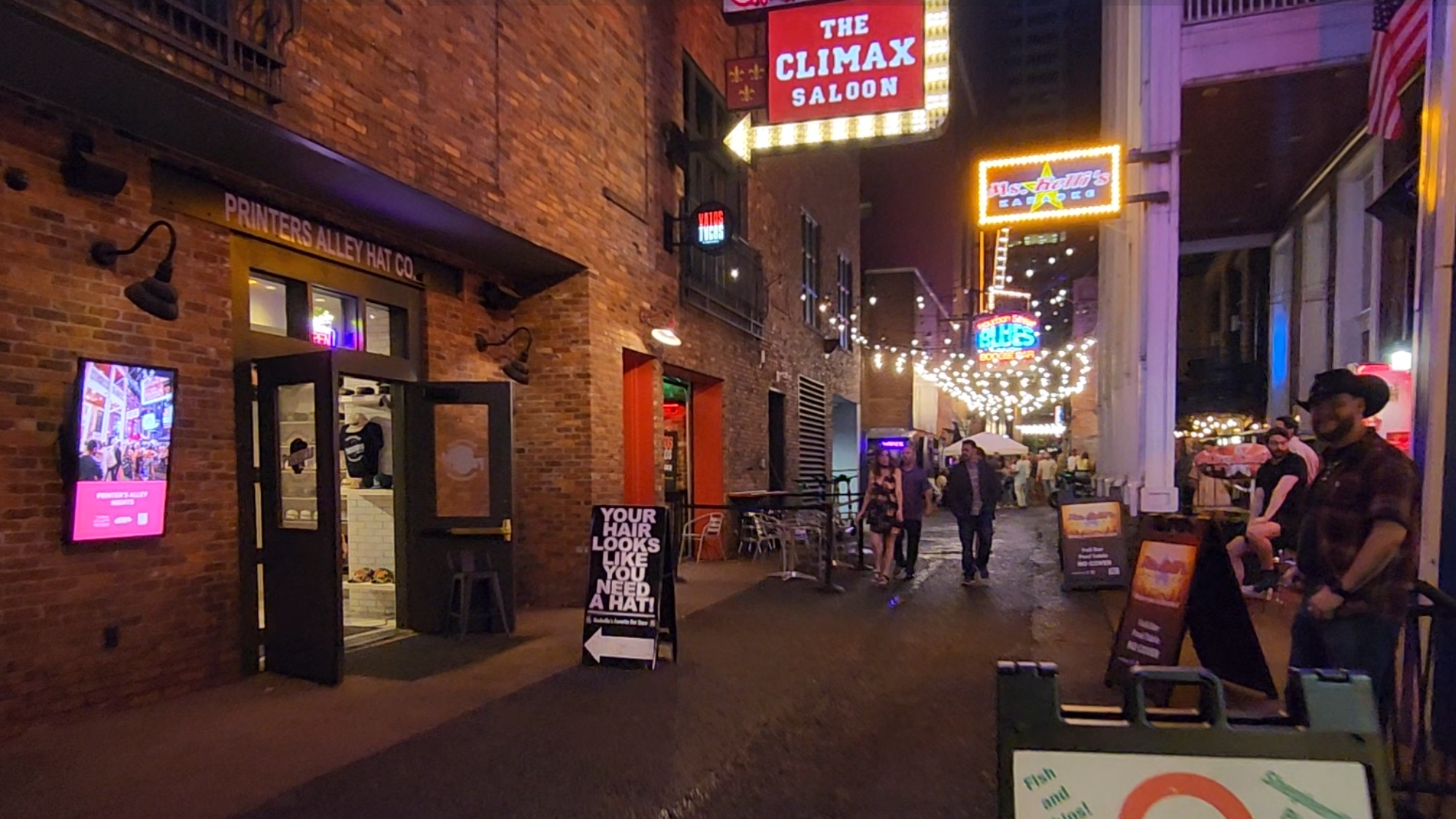 Neon bar signs illuminate Printer’s Alley at night.