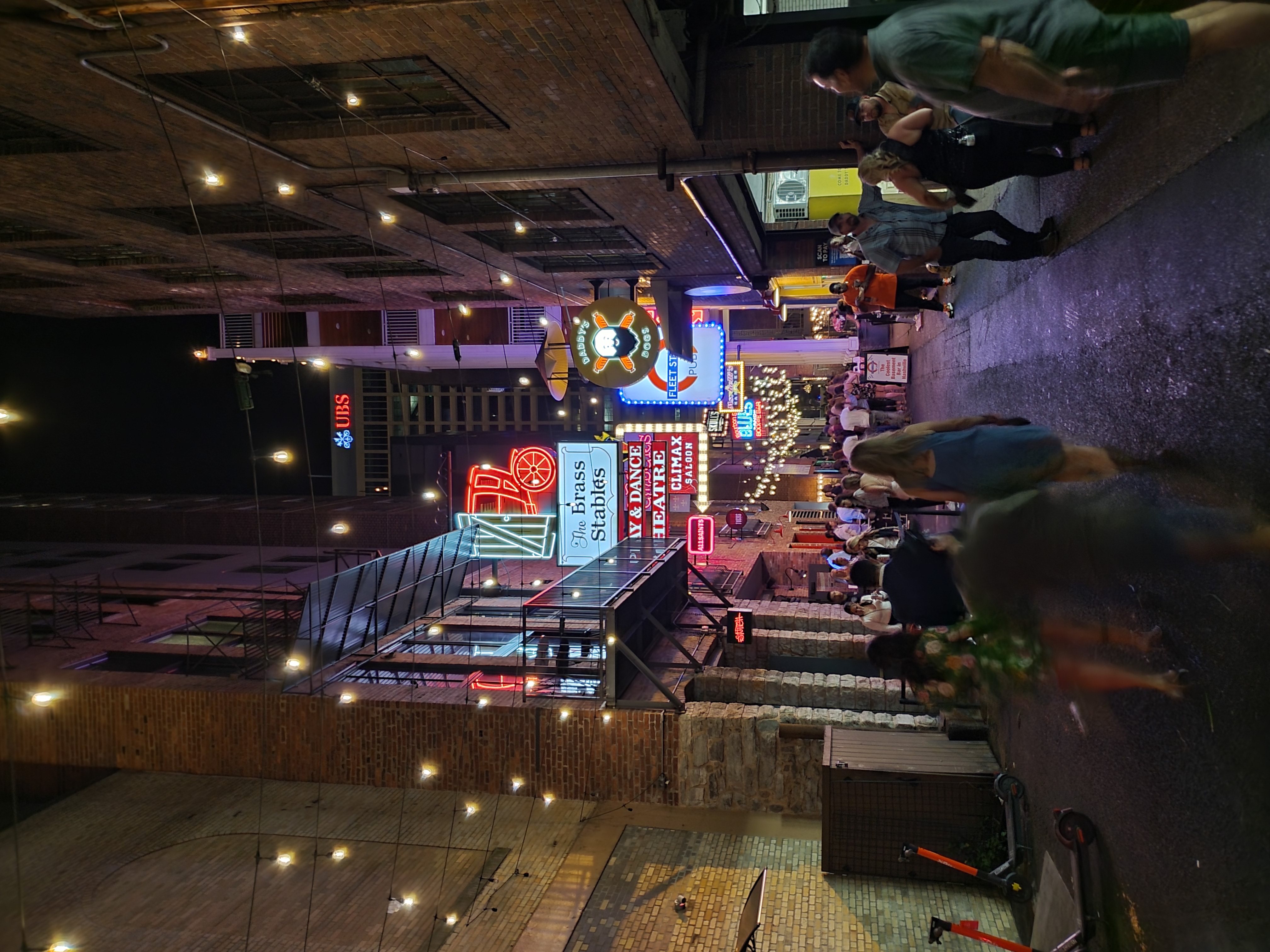 Visitors walk beneath neon bar signs and string lights in Printer’s Alley at night.
