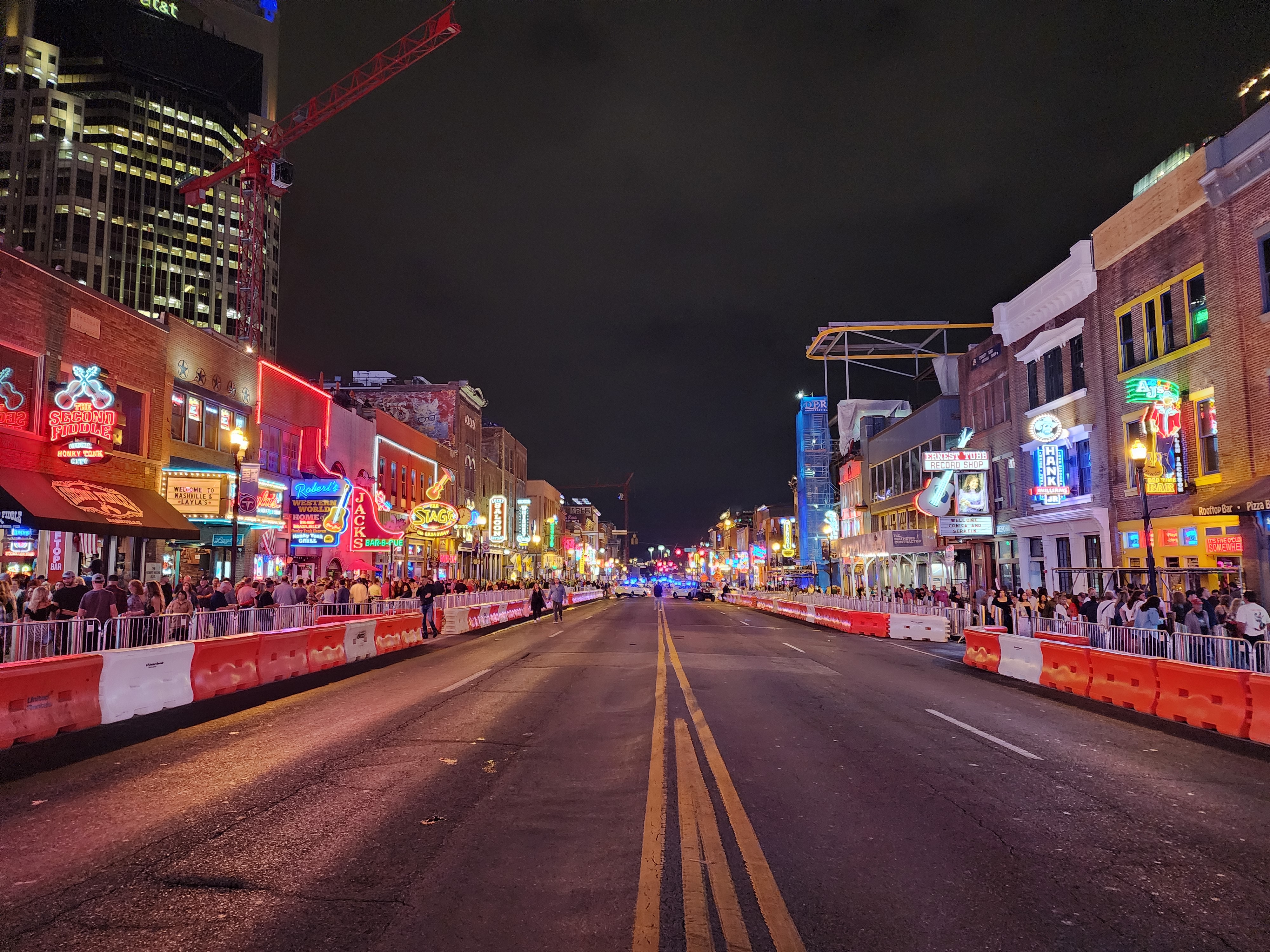 A wide view of Lower Broadway at night with traffic barriers along the roadway.