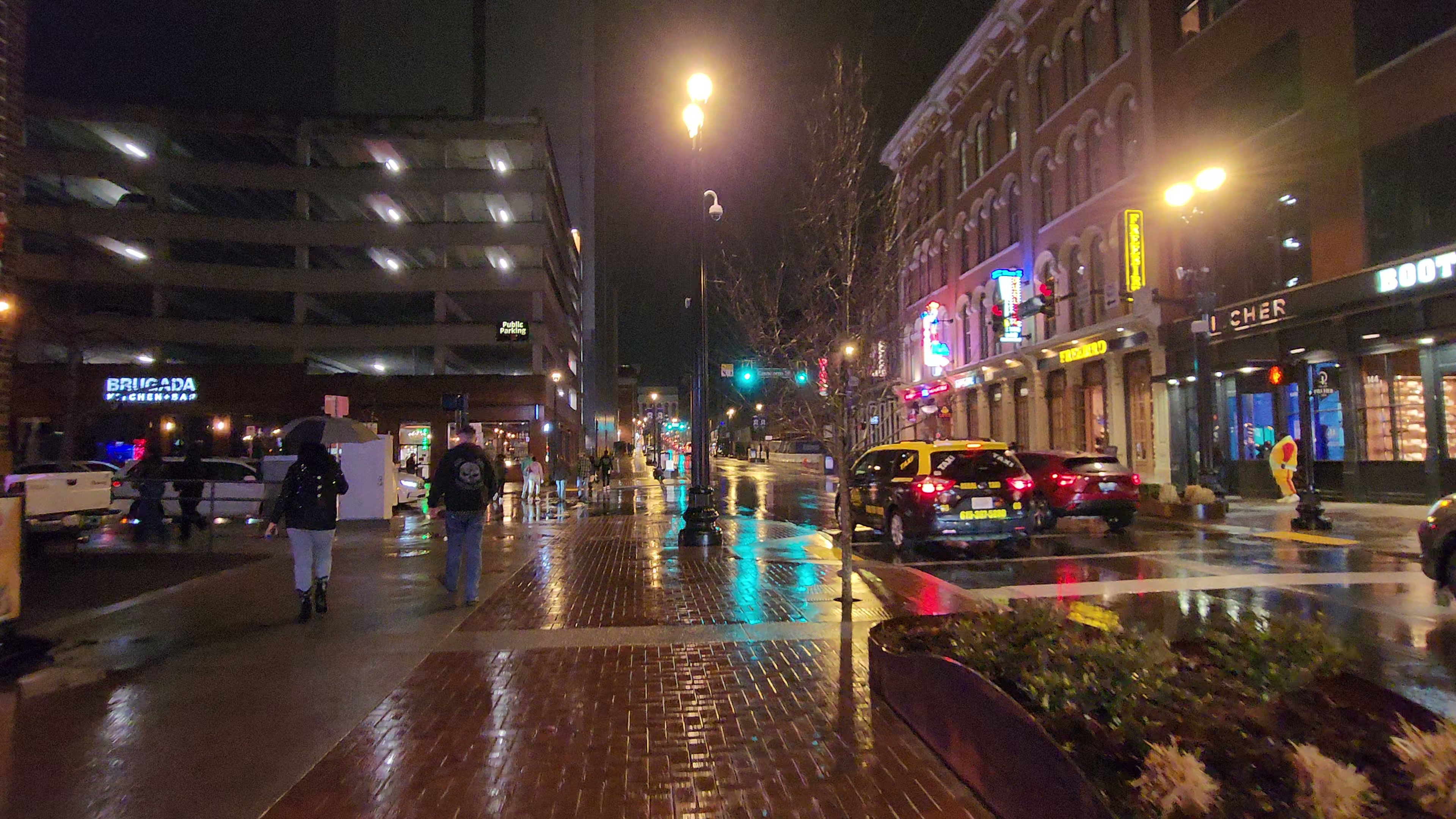 Lower Broadway glowing through rain and wet pavement at night.
